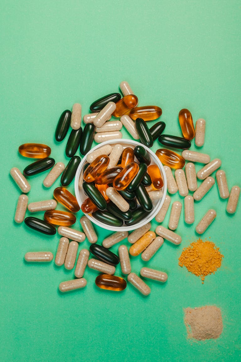 An assortment of capsules and powders on a green backdrop, symbolizing health and wellness.