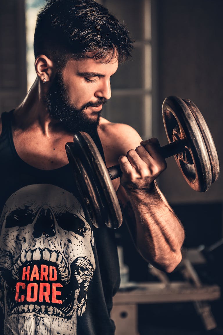 Bearded man in gym lifting a heavy dumbbell, showcasing strength and fitness.